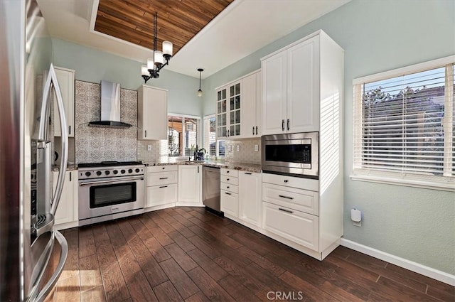 kitchen with dark wood-style floors, appliances with stainless steel finishes, light stone countertops, wall chimney range hood, and backsplash