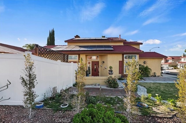 view of front of house featuring roof mounted solar panels, a tile roof, fence, and stucco siding