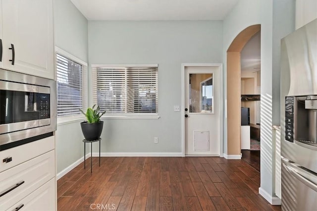 kitchen featuring arched walkways, white cabinets, baseboards, dark wood finished floors, and stainless steel appliances