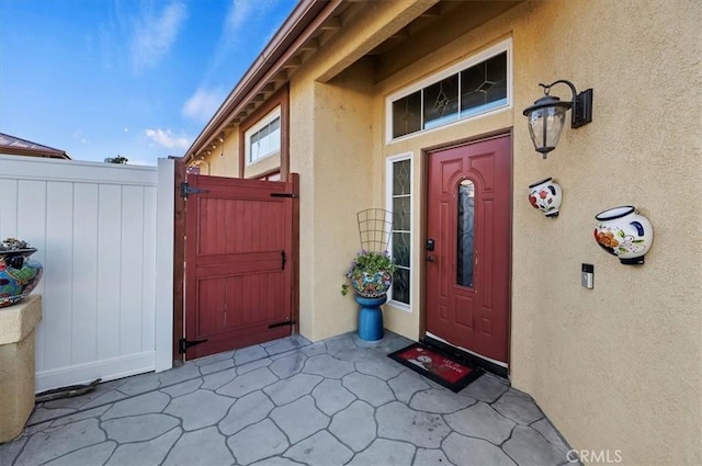 property entrance featuring fence, a gate, and stucco siding