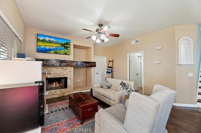 living room with visible vents, ceiling fan, a stone fireplace, wood finished floors, and baseboards