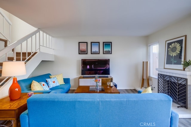 living area featuring wood finished floors, a fireplace with raised hearth, baseboards, and stairs