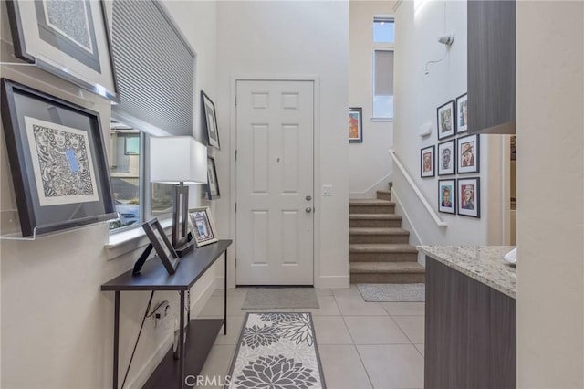 foyer entrance featuring light tile patterned floors, stairway, plenty of natural light, and baseboards