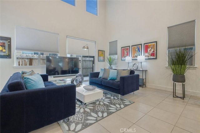 tiled living area featuring a healthy amount of sunlight, a towering ceiling, and baseboards