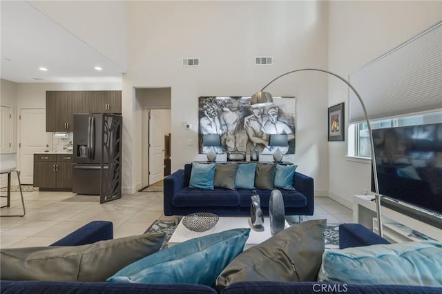 living area with light tile patterned floors, baseboards, a high ceiling, and visible vents