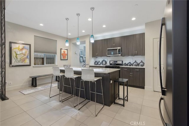 kitchen with a center island with sink, appliances with stainless steel finishes, light countertops, dark brown cabinets, and a kitchen bar