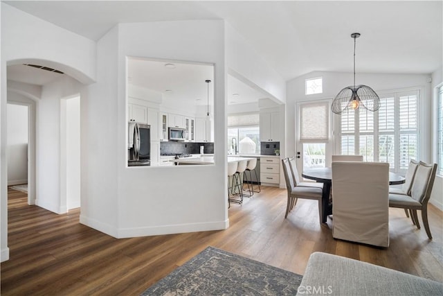 dining area with arched walkways, visible vents, vaulted ceiling, wood finished floors, and baseboards