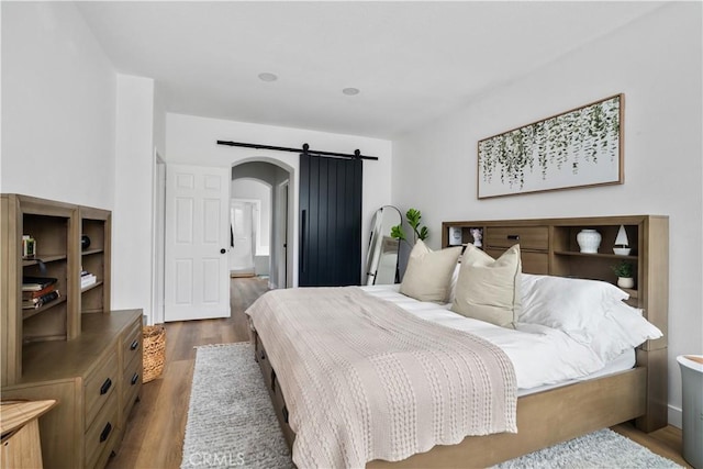 bedroom featuring arched walkways, wood finished floors, and a barn door