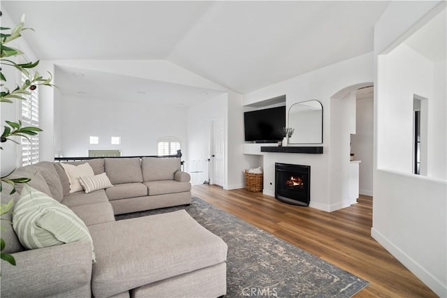 living area featuring lofted ceiling, a lit fireplace, baseboards, and wood finished floors