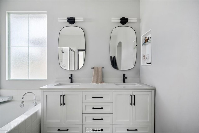 bathroom with tiled bath, a sink, and double vanity