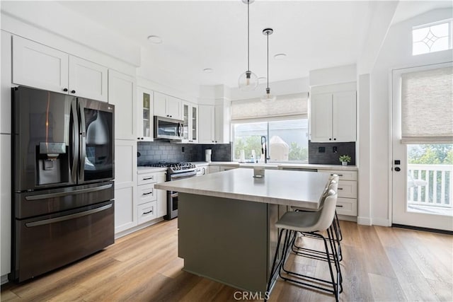 kitchen featuring stainless steel appliances, white cabinets, light countertops, light wood-type flooring, and glass insert cabinets