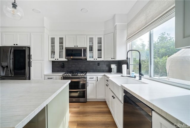 kitchen with appliances with stainless steel finishes, wood finished floors, light countertops, white cabinetry, and a sink