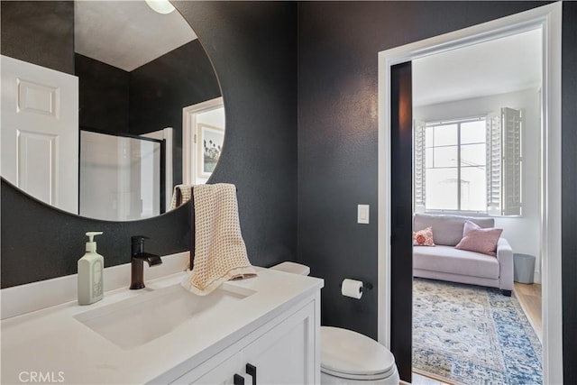 full bath with a textured wall, toilet, connected bathroom, a shower stall, and vanity