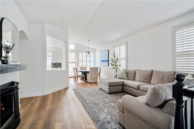 living area with a warm lit fireplace, baseboards, vaulted ceiling, and wood finished floors