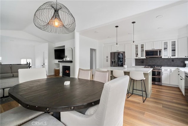 dining room with a warm lit fireplace, light wood finished floors, and lofted ceiling