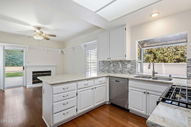 kitchen with tasteful backsplash, stainless steel dishwasher, a brick fireplace, a sink, and a peninsula