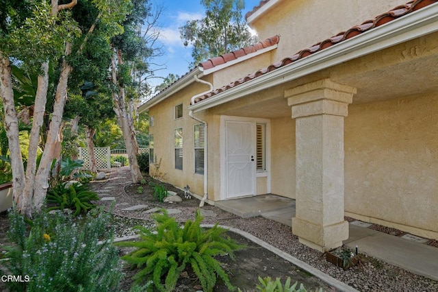 doorway to property featuring stucco siding, a tile roof, and fence