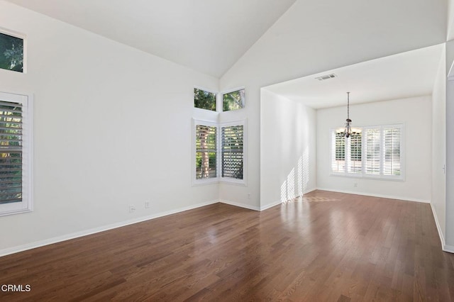 empty room featuring a wealth of natural light, dark wood-style flooring, visible vents, and a notable chandelier