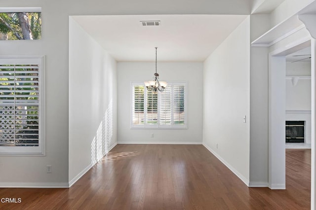 unfurnished dining area featuring a chandelier, wood finished floors, a fireplace with flush hearth, visible vents, and baseboards