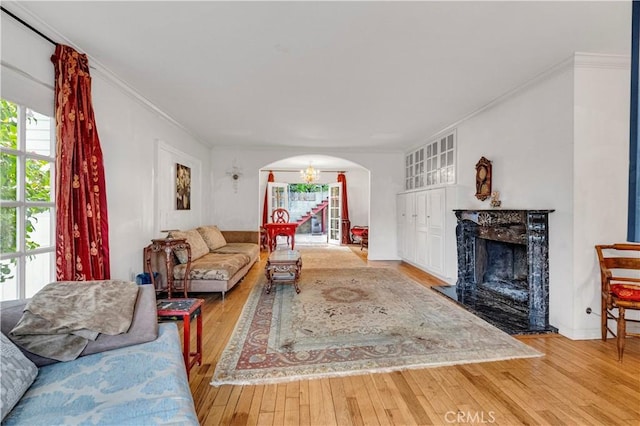 living room with hardwood / wood-style flooring, a premium fireplace, arched walkways, and crown molding