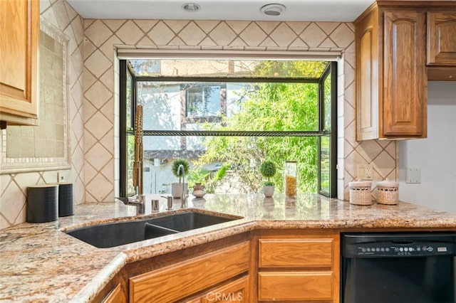 kitchen with light stone counters, black dishwasher, a sink, and backsplash