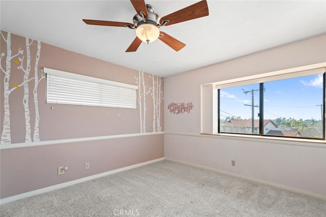 carpeted spare room featuring ceiling fan and baseboards