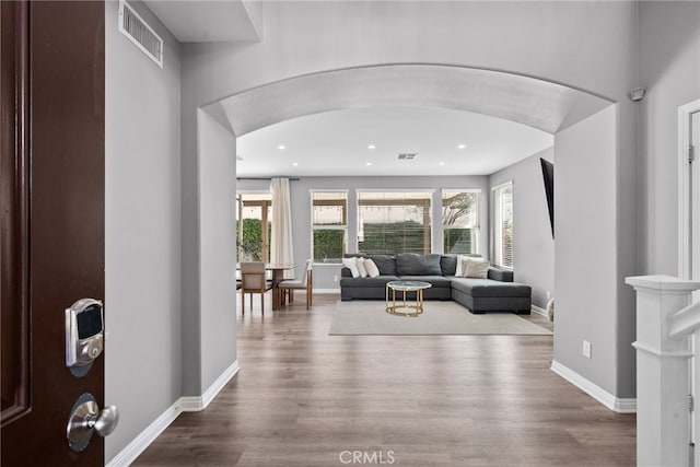 living room with arched walkways, wood finished floors, visible vents, and baseboards