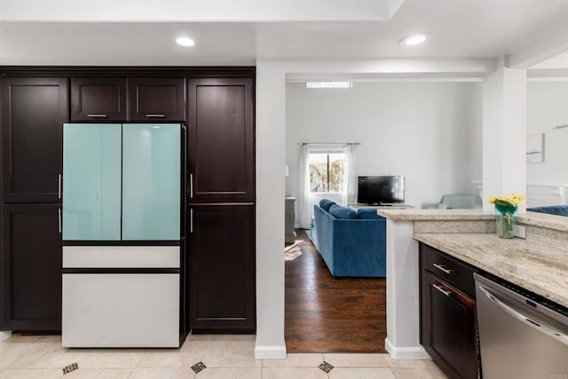 kitchen featuring light stone counters, light tile patterned floors, stainless steel dishwasher, freestanding refrigerator, and dark brown cabinets