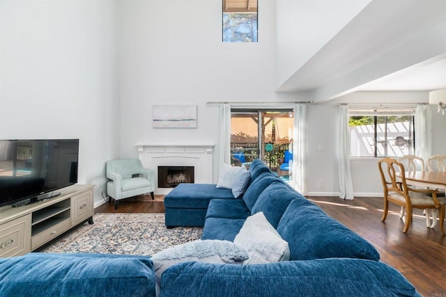 living area featuring a high ceiling, a fireplace, baseboards, and wood finished floors