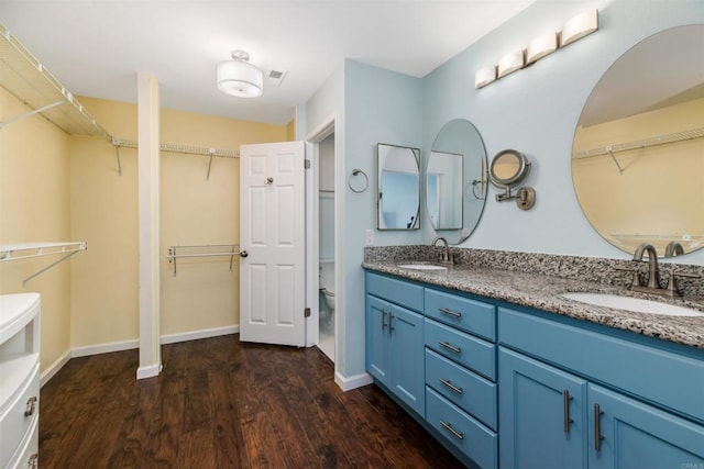 full bathroom featuring toilet, double vanity, a sink, and wood finished floors