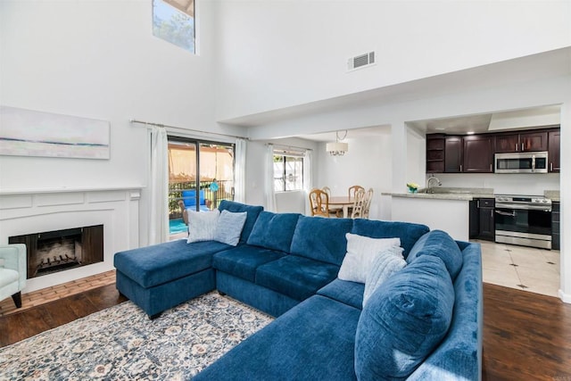 living area with a towering ceiling, a fireplace, visible vents, and dark wood-type flooring