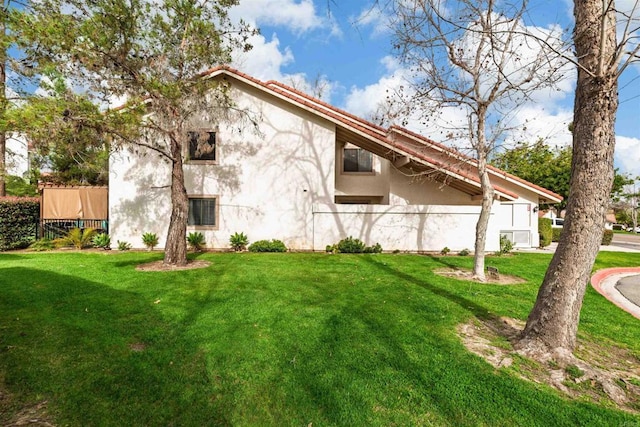 exterior space with a tile roof, fence, a lawn, and stucco siding