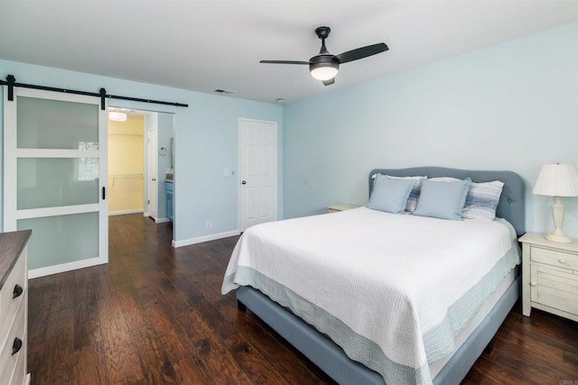 bedroom featuring a barn door, visible vents, baseboards, a ceiling fan, and wood finished floors