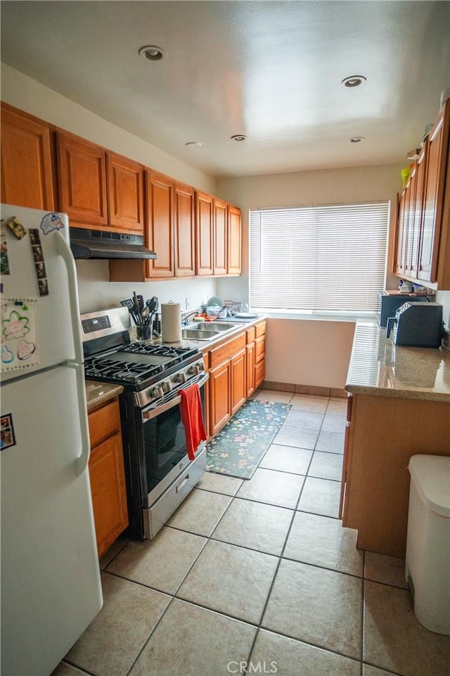 kitchen with under cabinet range hood, gas stove, plenty of natural light, and freestanding refrigerator