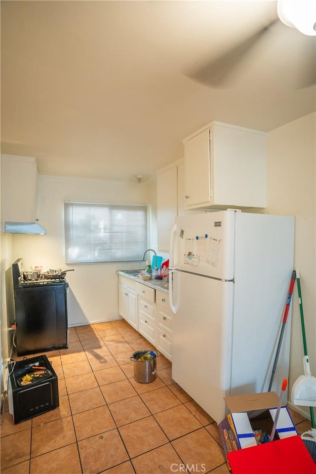 kitchen with stainless steel range with gas cooktop, light tile patterned floors, freestanding refrigerator, white cabinetry, and a sink