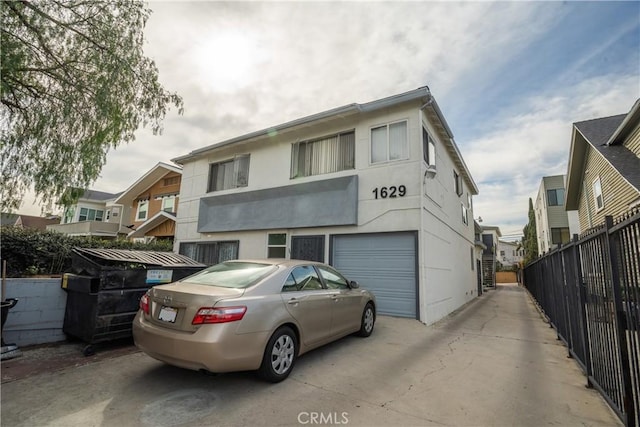 view of property with fence, driveway, an attached garage, and stucco siding