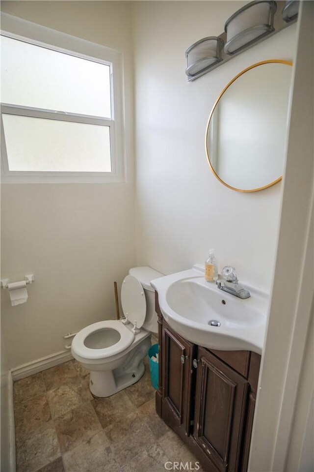 bathroom featuring baseboards, stone finish flooring, toilet, and vanity