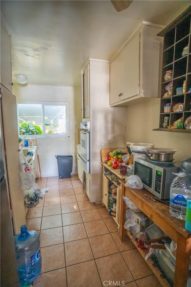 kitchen with stainless steel microwave, light tile patterned flooring, oven, and white cabinetry