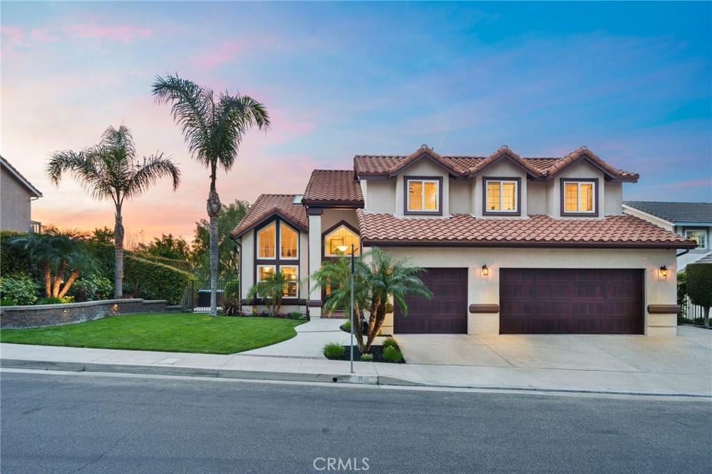 view of front of home with concrete driveway, a lawn, a tile roof, and stucco siding