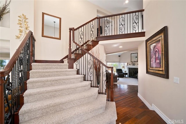 stairway with hardwood / wood-style flooring, recessed lighting, a high ceiling, a fireplace, and baseboards