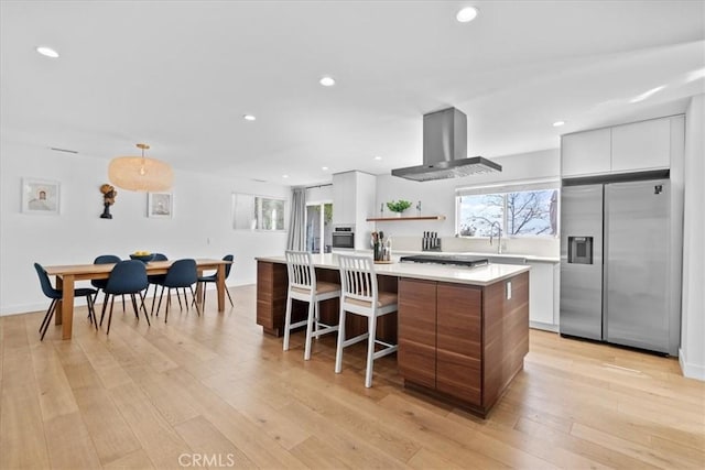 kitchen with stainless steel appliances, light countertops, ventilation hood, modern cabinets, and light wood-type flooring