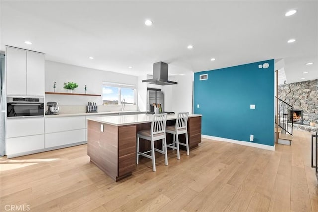 kitchen featuring light wood-style flooring, modern cabinets, appliances with stainless steel finishes, extractor fan, and white cabinetry