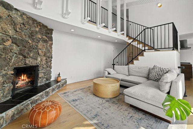 living area with a fireplace, stairway, a towering ceiling, and wood finished floors