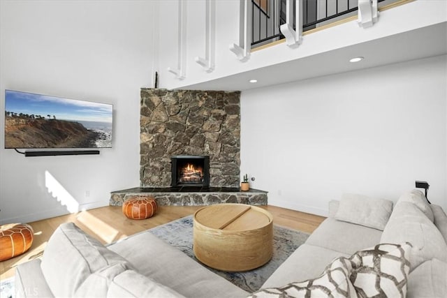 living area featuring a high ceiling, a fireplace, baseboards, and wood finished floors