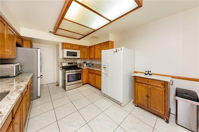 kitchen with light stone counters, white appliances, visible vents, backsplash, and brown cabinetry