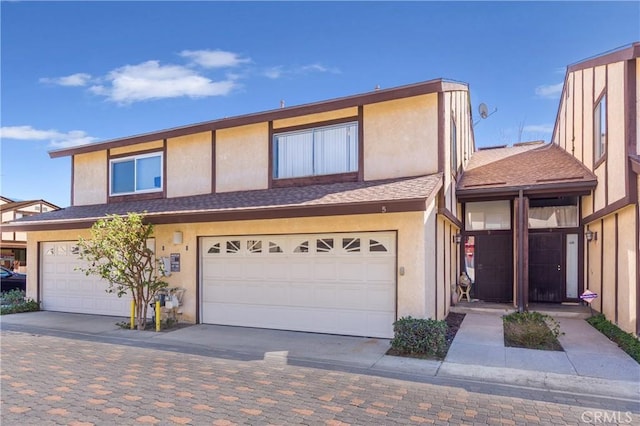 view of front of house featuring roof with shingles, driveway, an attached garage, and stucco siding