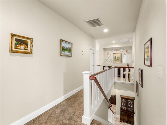 hall with baseboards, visible vents, and an upstairs landing