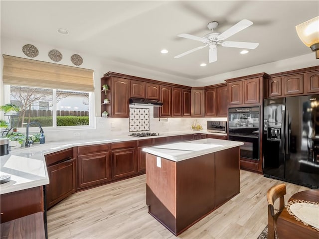 kitchen featuring light countertops, a sink, under cabinet range hood, and black appliances