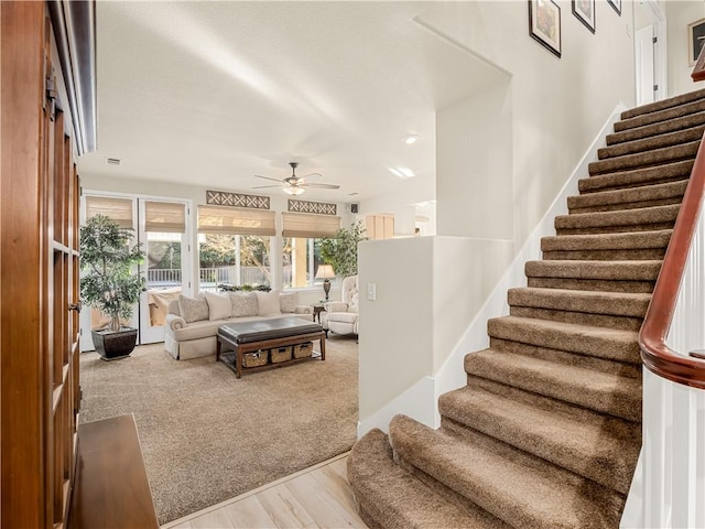 living room featuring a ceiling fan, carpet, stairway, and wood finished floors