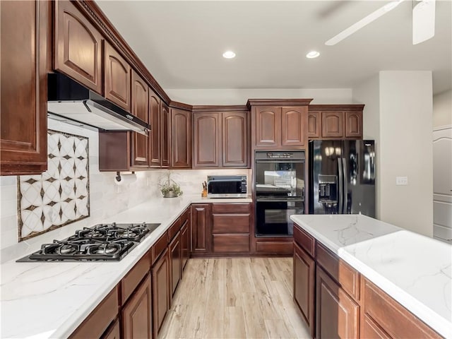 kitchen with light stone counters, tasteful backsplash, light wood-type flooring, under cabinet range hood, and black appliances